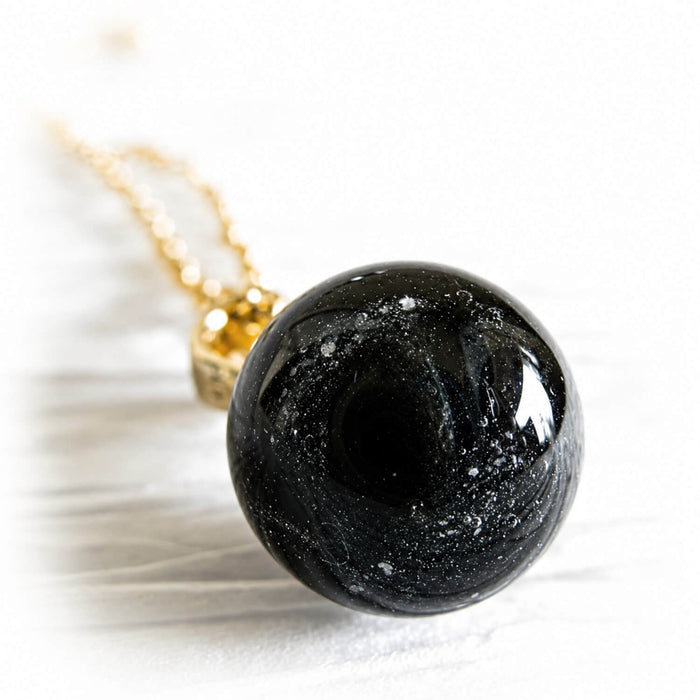 Closeup of a black glass memorial marble on a 14k gold pendant and chain