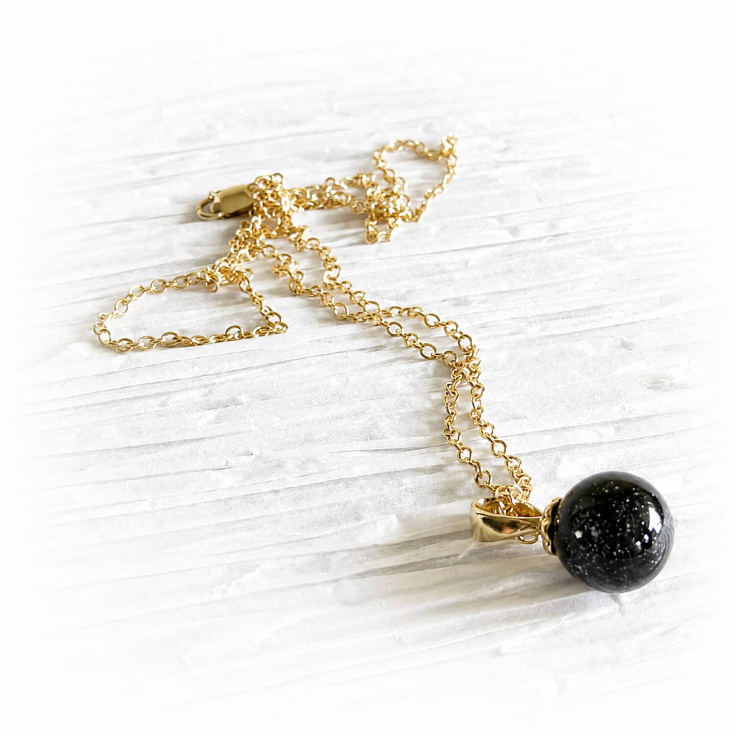 Hand-blown black glass marble with cremation ashes on a 14k gold chain shown on a white background 