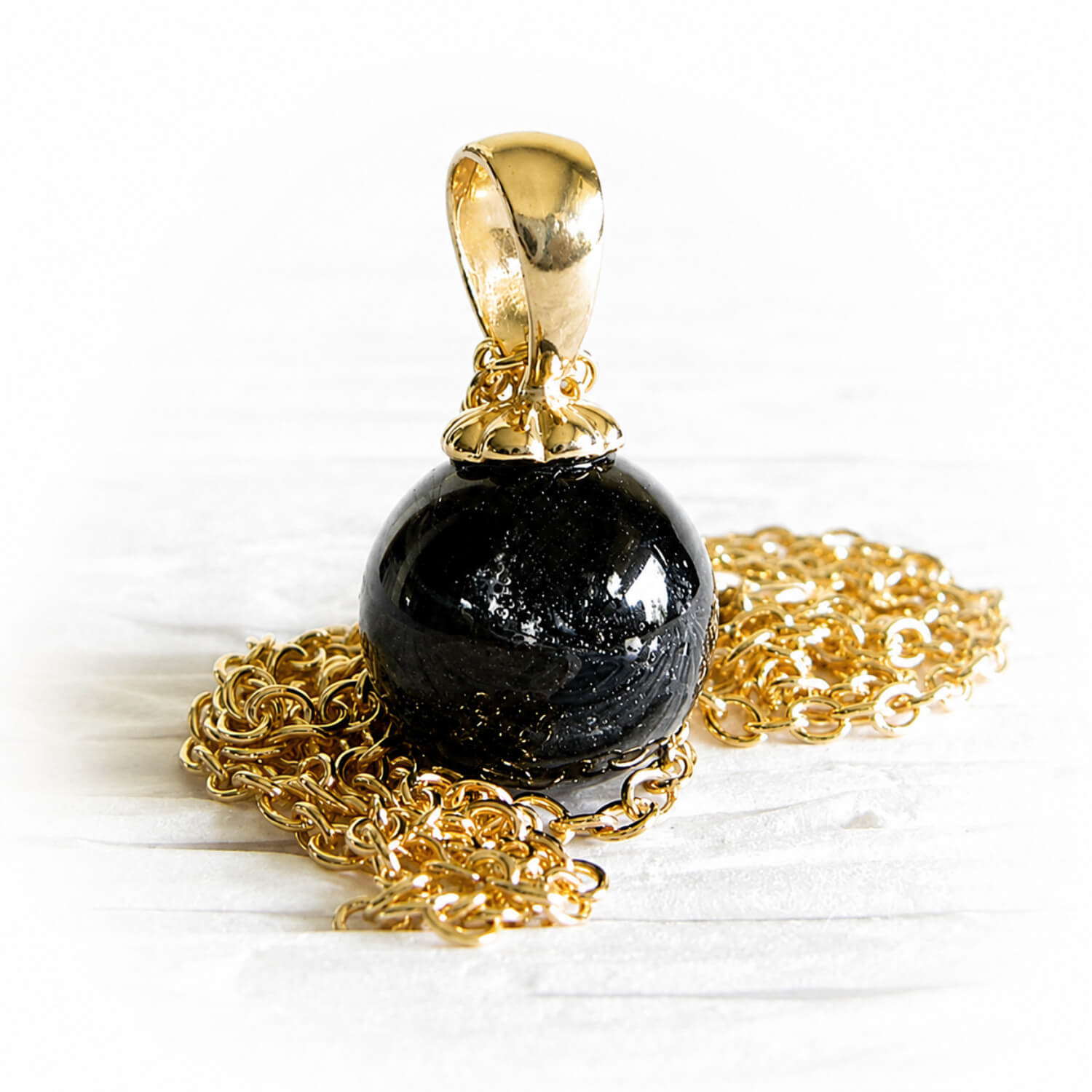 Small cremation marble with swirled ashes set on a 14k gold pendant and a gold chain