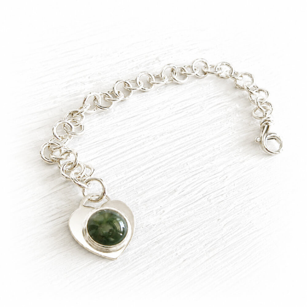 Hand crafted sterling silver charm bracelet with a heart-shaped focal charm featuring a green hand blown glass infused with cremation ashes