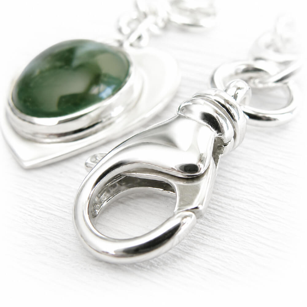 Close up of a high quality sterling silver lobster clasp on an artisan crafted charm bracelet with a green glass cremation cabochon 
