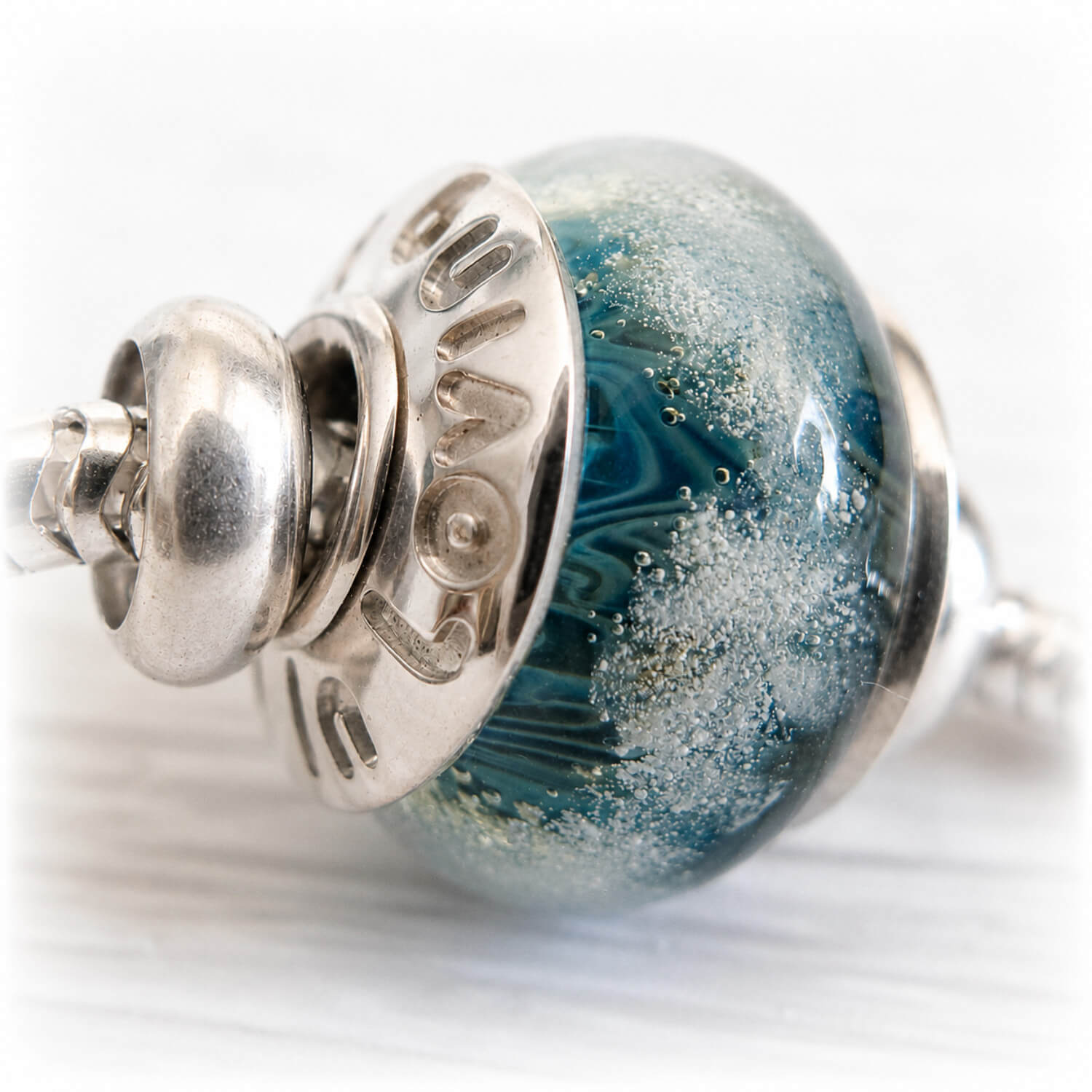Cremation ashes suspended in a hand blown glass bead with custom engraving on sterling silver bead caps