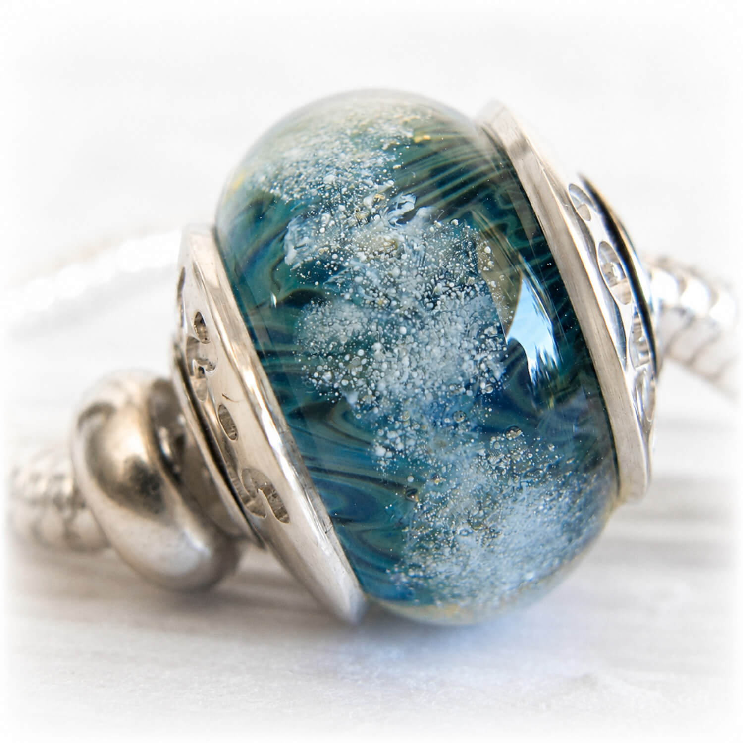 Hand blown glass bead with shades of blue showcasing floating ashes visible within the glass
