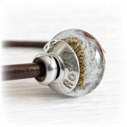 Memorial bead containing cremation ashes encased in hand blown glass on a brown leather bracelet