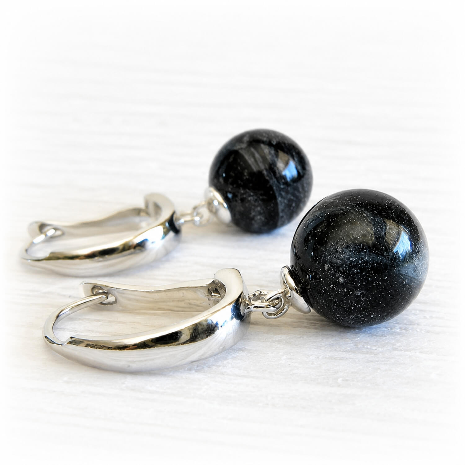 Pair of sterling silver earrings with black memorial ash marbles on a white background