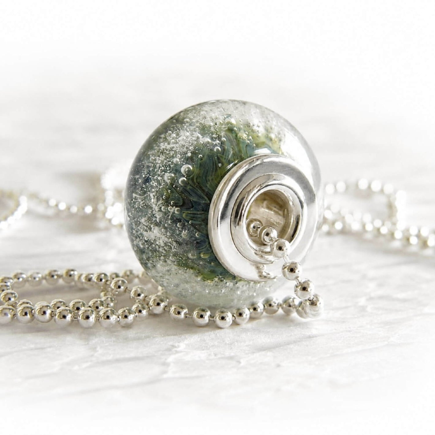 Handcrafted memorial glass cremation bead with ashes suspended within the glass on a sterling silver bead chain