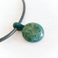 Hand blown glass cremation pendant with swirls of teal, aqua and cremation ashes on a black leather chord