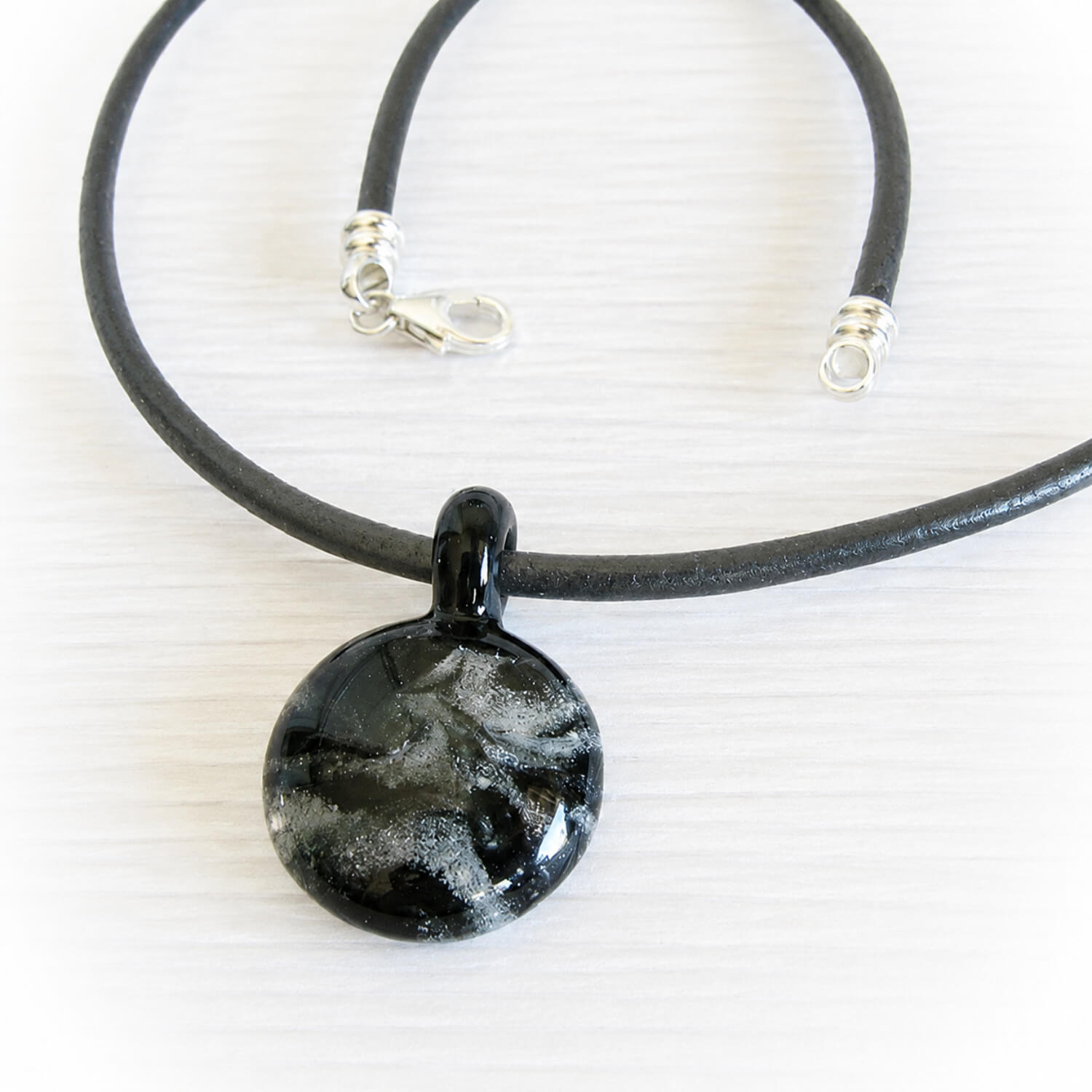 White cremation ashes encased in a black hand blown glass memorial pendant on a black leather chord