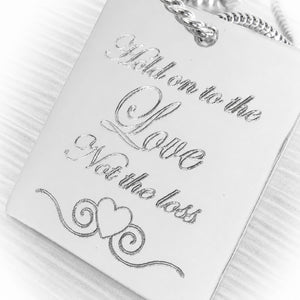 Custom engraving on the back of a sterling silver memorial necklace that says 'Hold on to the Love Not the loss' and a heart scroll design