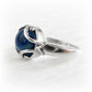 A sterling silver ring featuring a blue glass cremation cabochon, set in an abstract, organic-shaped band on a white textured background.