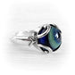 A sterling silver ring featuring a round cremation glass cabochon with a deep blue and green iridescent pattern, set in a decorative swirl design on a white background.