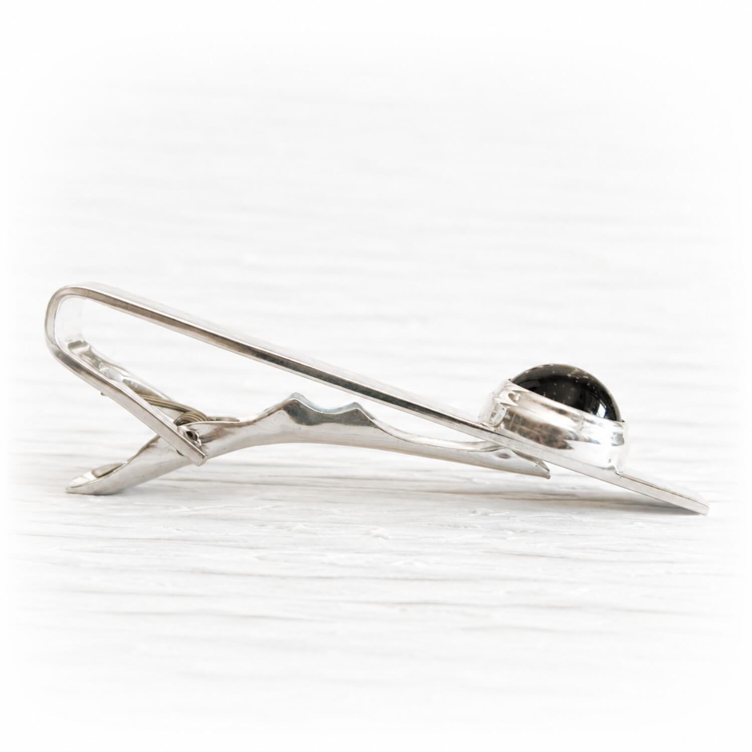 Side view of a sterling silver memorial tie bar with a black glass cabochon infused with cremation ashes
