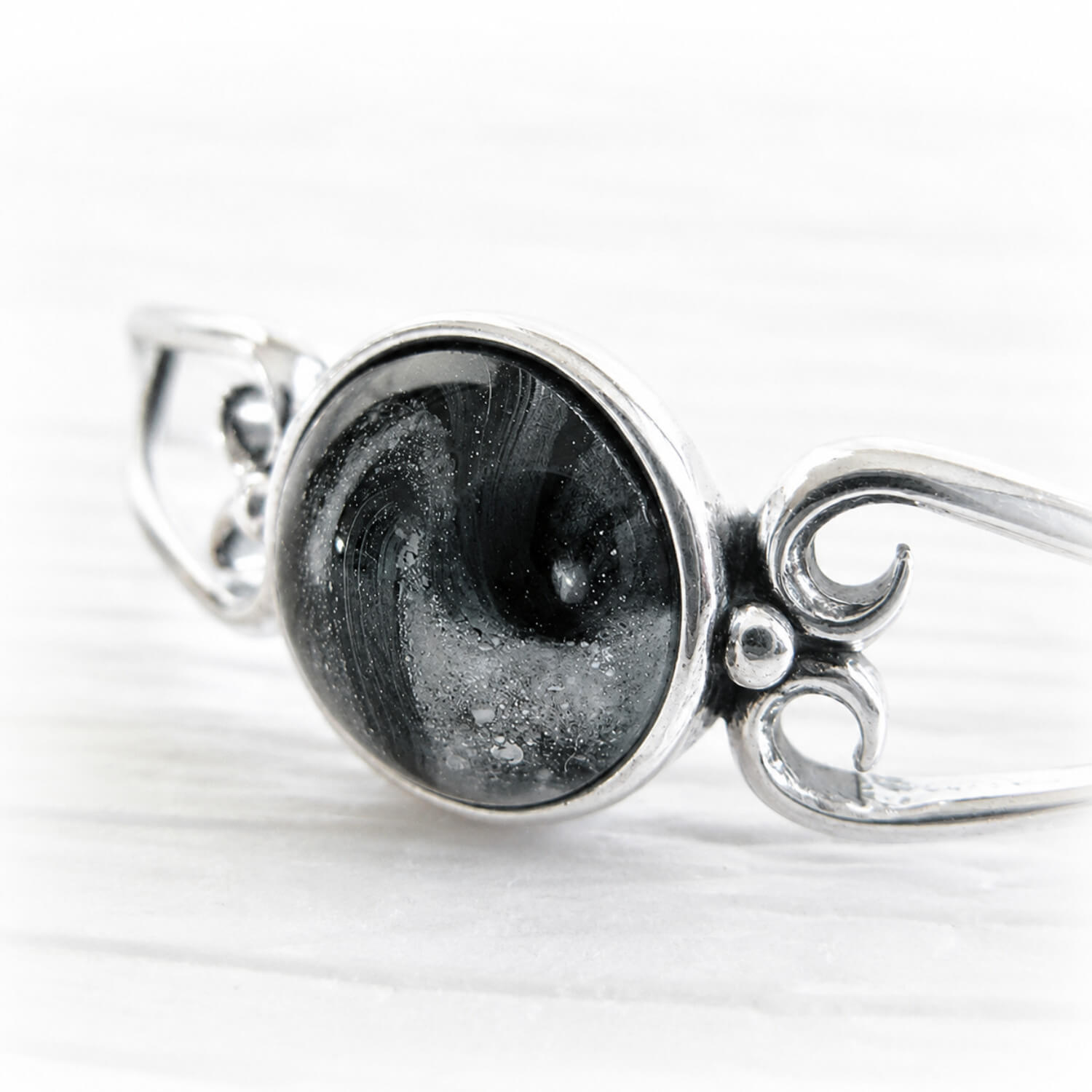 White cremation ashes swirled with black hand blown glass centered in a sterling silver memorial cuff bracelet