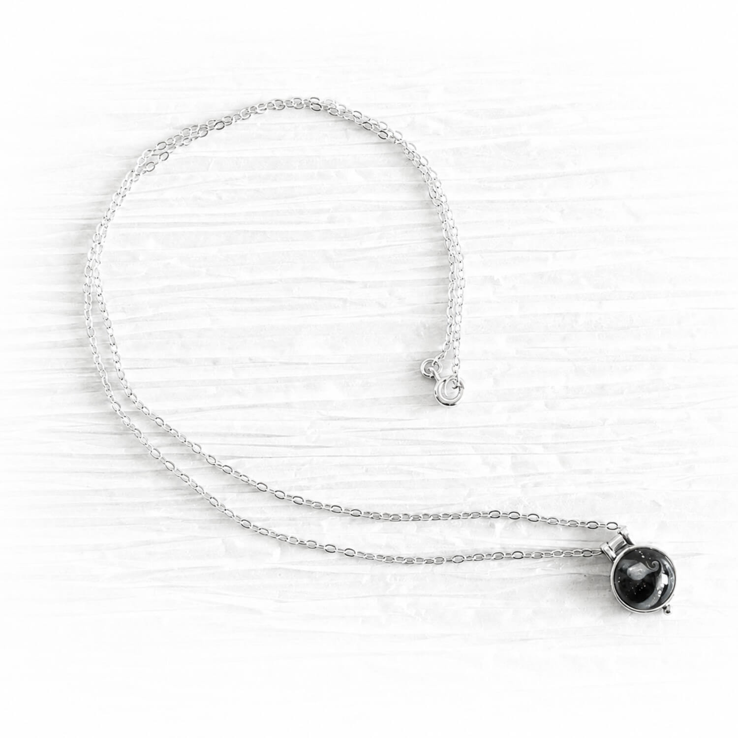 Black hand blown glass mixed with white cremation ashes set in a tiny sterling silver memorial pendant