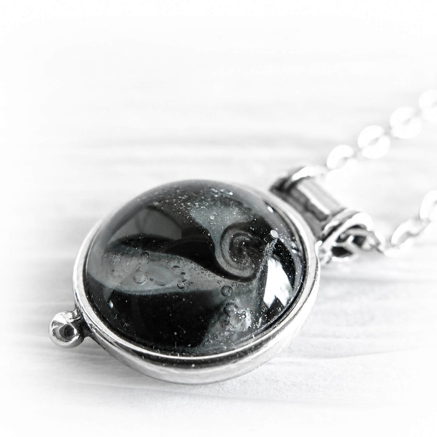 Close up of white cremation ashes encased in black hand blown glass on a dainty sterling silver memorial pendant