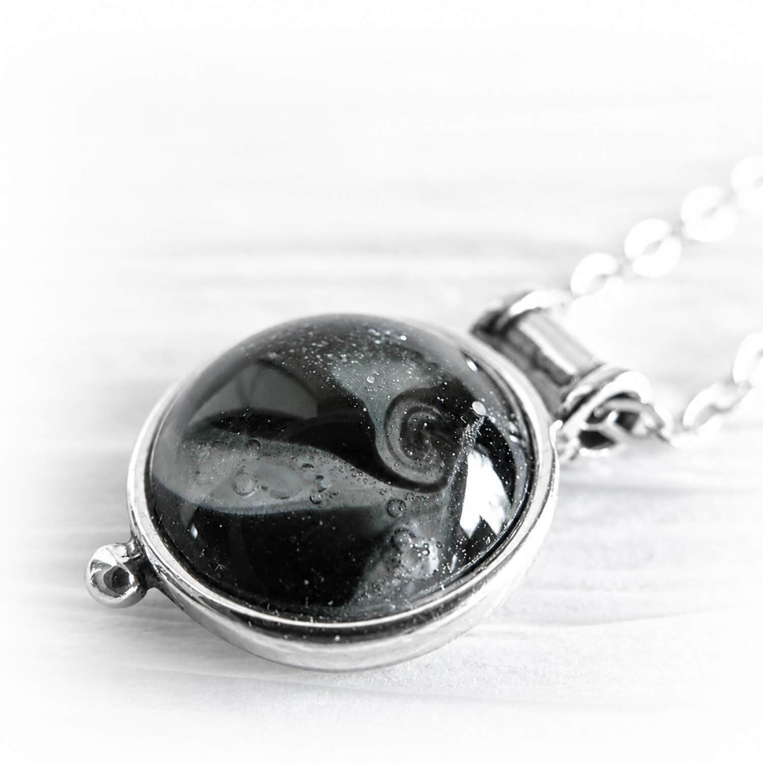 Close up of white cremation ashes encased in black hand blown glass on a dainty sterling silver memorial pendant