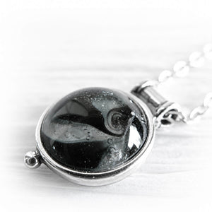 Close up of white cremation ashes encased in black hand blown glass on a dainty sterling silver memorial pendant