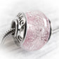 Close-up of a pink glass cremation ash memorial bead necklace with silver metal component on a white background