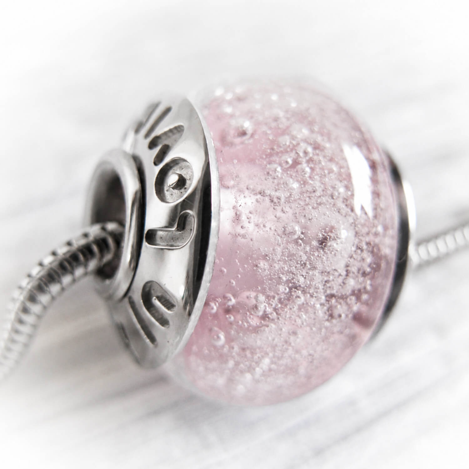 Close-up of a pink glass cremation ash memorial bead necklace with silver metal component on a white background