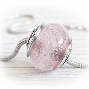 Pink glass cremation memorial bead with silver setting on a white background