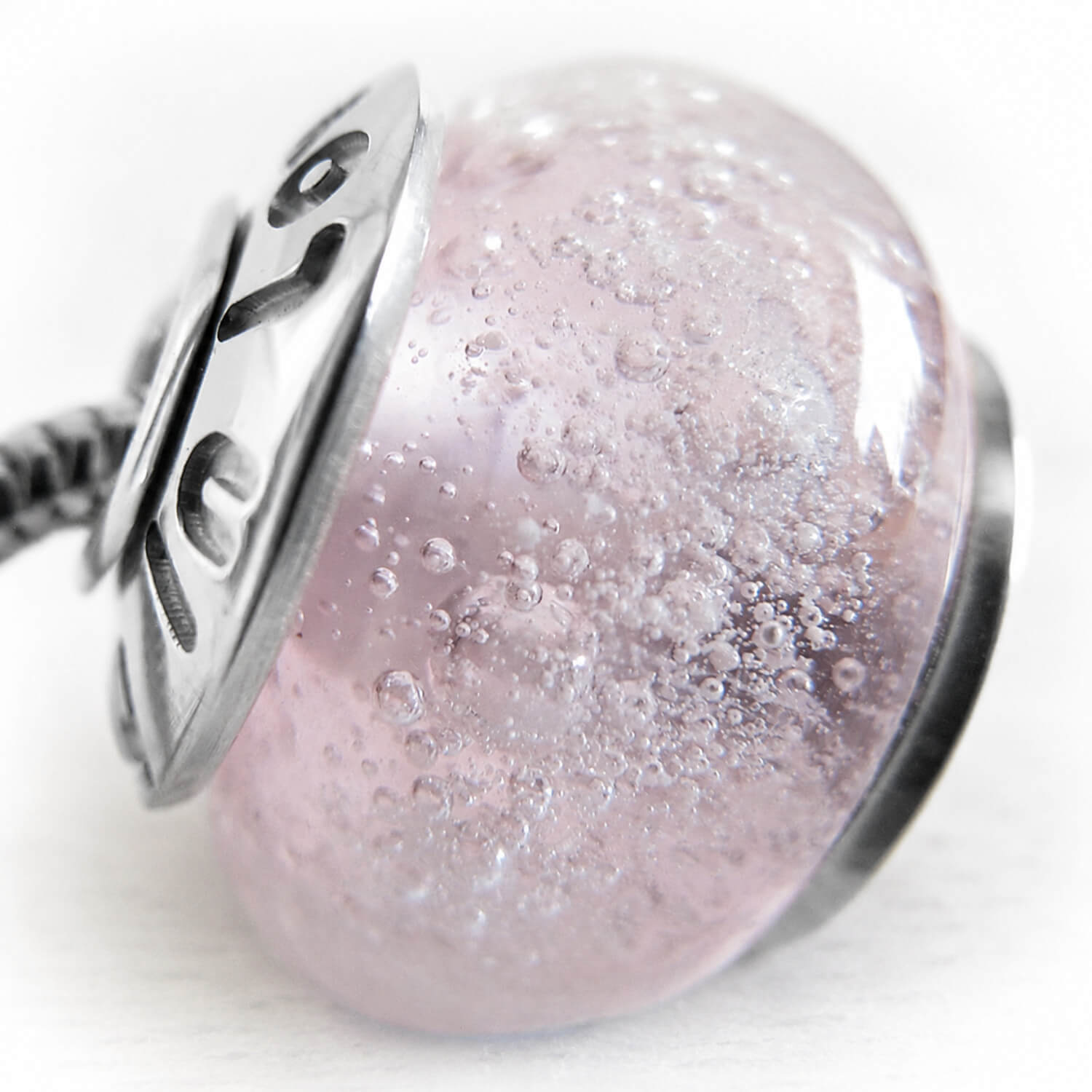 Close-up of a pink glass bead with silver accents and cremation ashes on a white background