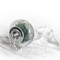 Green and blue swirled artisan-crafted  glass focal bead with floating ashes visible within the glass on a sterling silver bead chain