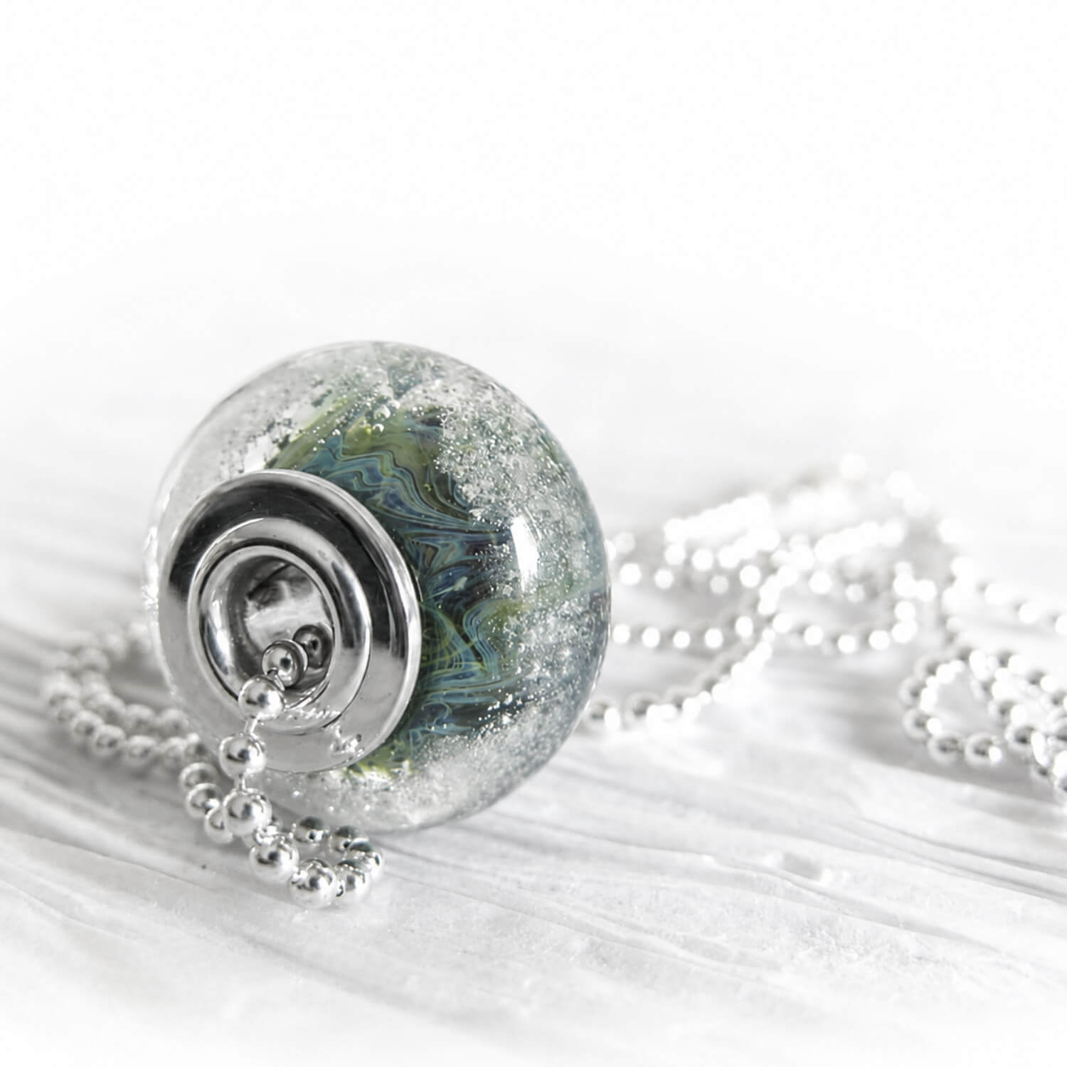 Green and blue swirled artisan-crafted  glass focal bead with floating ashes visible within the glass on a sterling silver bead chain