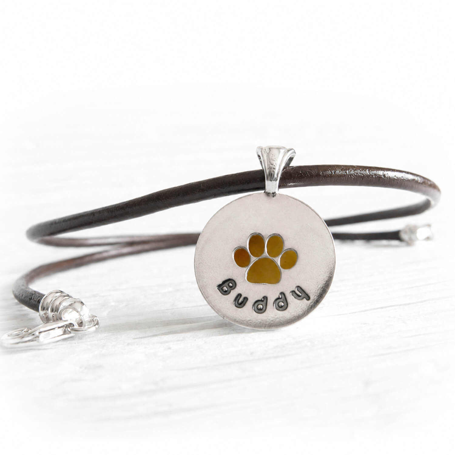 Sterling silver pet memorial necklace with custom engraving and a paw print cutout on a leather chord