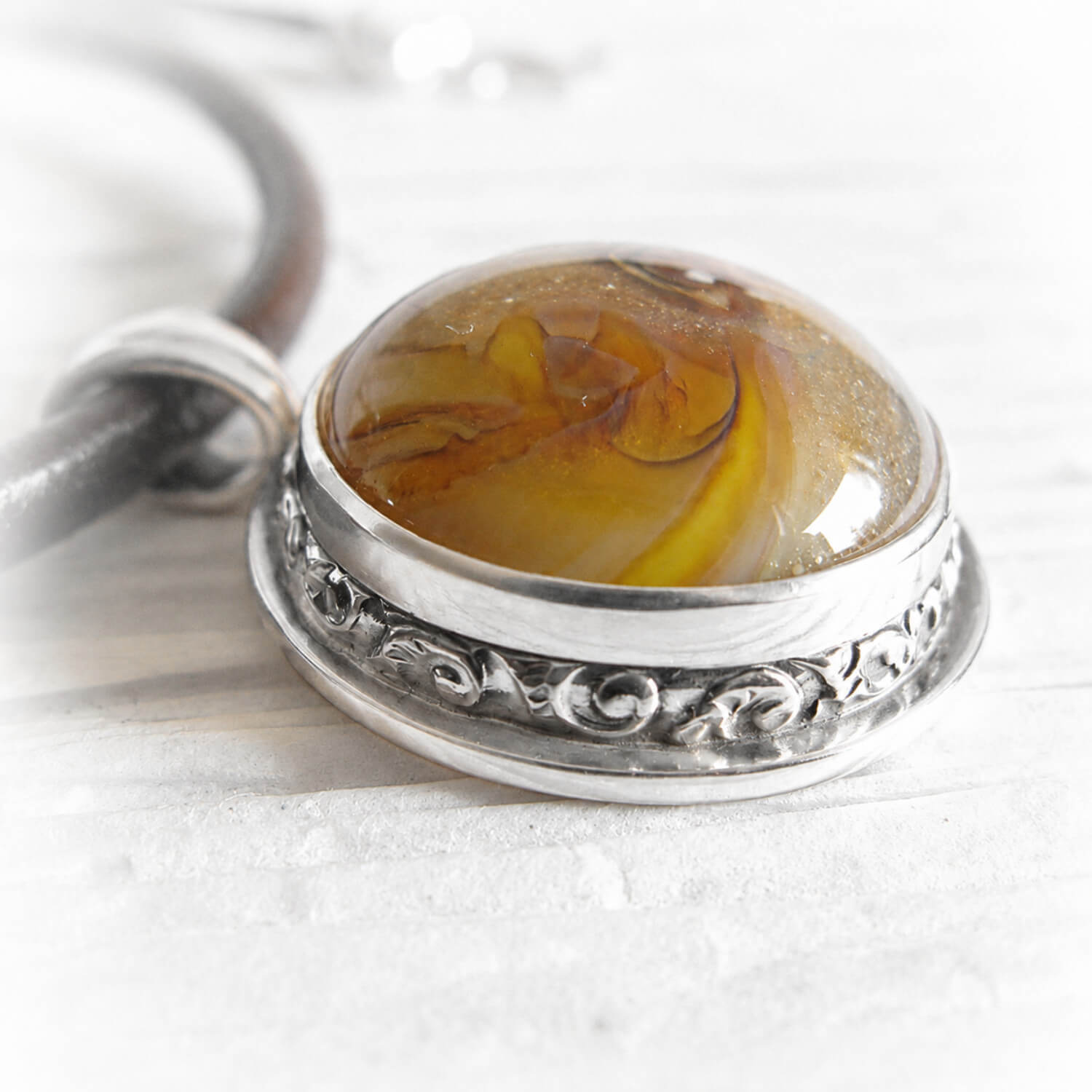 Pet memorial glass containing ashes with a sterling silver pendant on a brown leather chord
