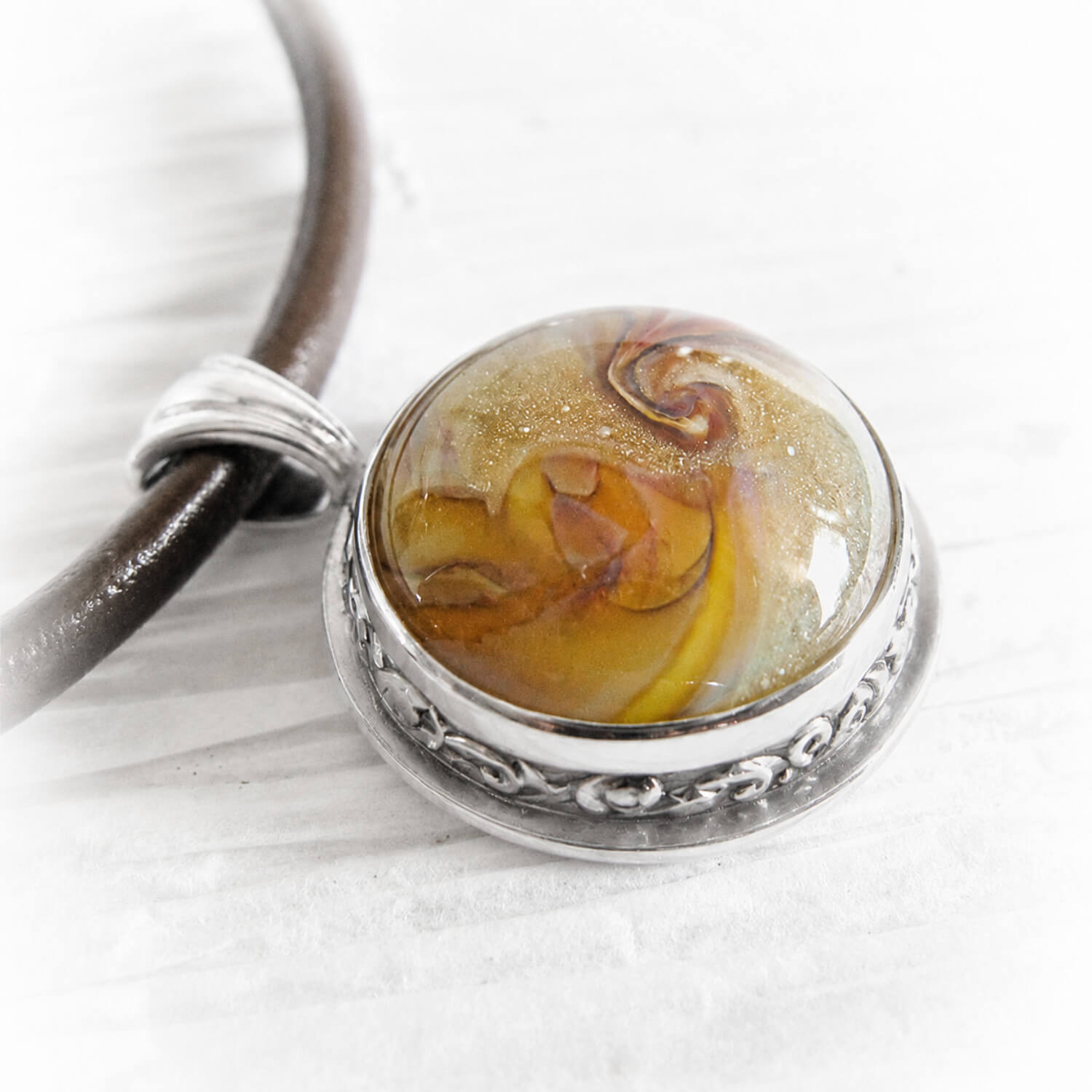 Amber and yellow hand blown glass swirled with cremation ashes set into a sterling silver pendant 