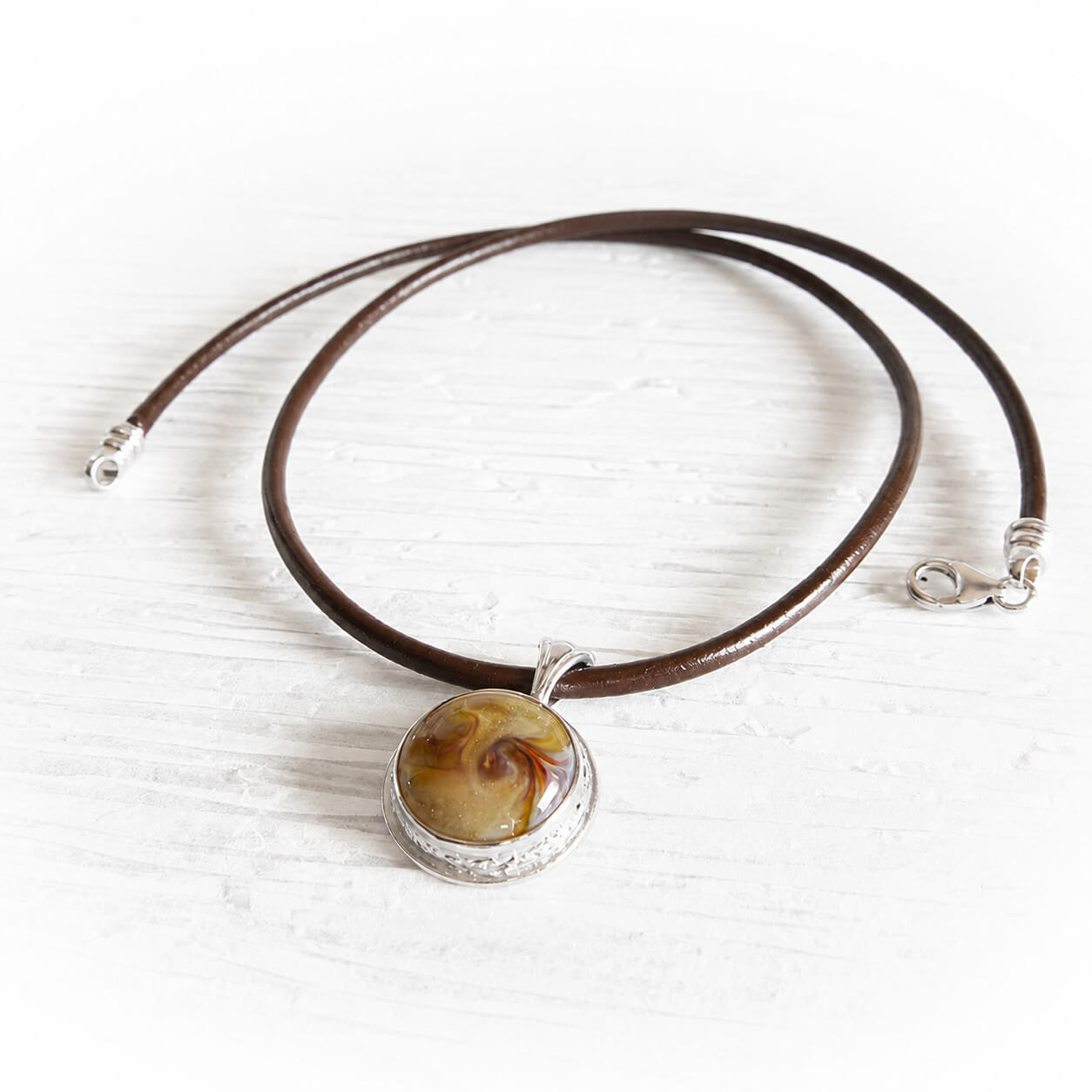 Pet memorial necklace with a circular glass cremation gemstone set in sterling silver in a brown leather chord