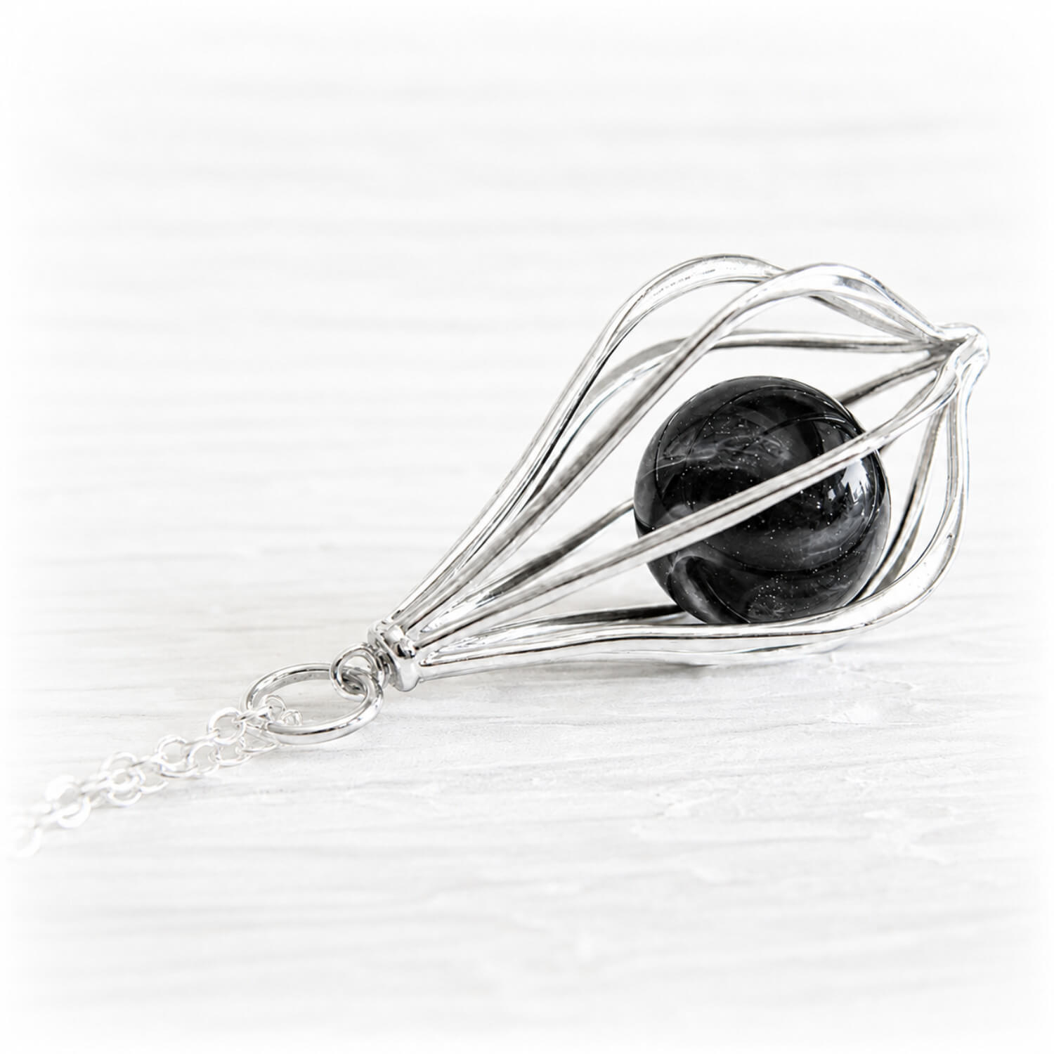 Sterling silver cage pendant featuring a black glass marble swirled with cremation ashes