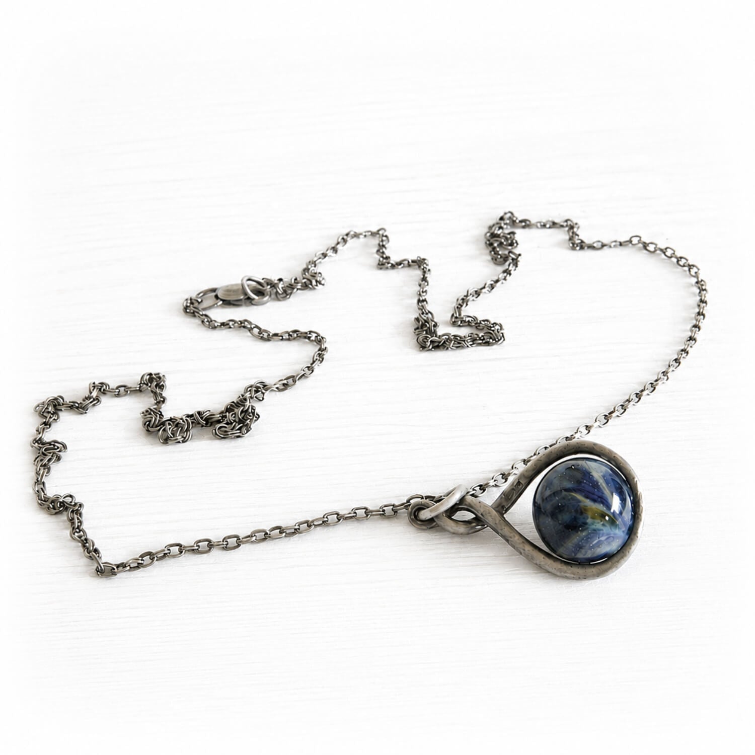 Sterling silver necklace with an antique finish featuring a blue artisan made glass marble containing cremation ashes