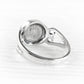 A silver ring with a polished bezel setting, shown from a side angle on a light, textured white surface.