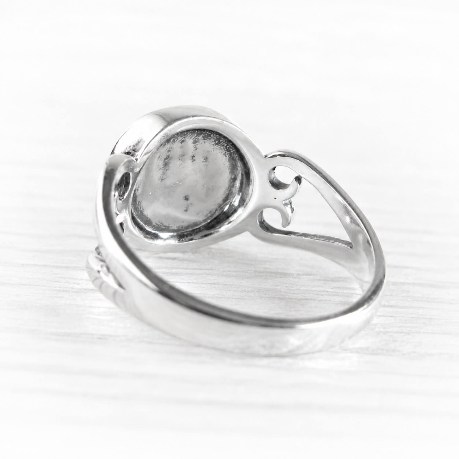 A silver ring with a polished bezel setting, shown from a side angle on a light, textured white surface.