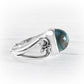 A silver ring featuring a polished dome-shaped cremation glass cabochon stone with iridescent blue, green, and gold patterns, set on a white textured background.