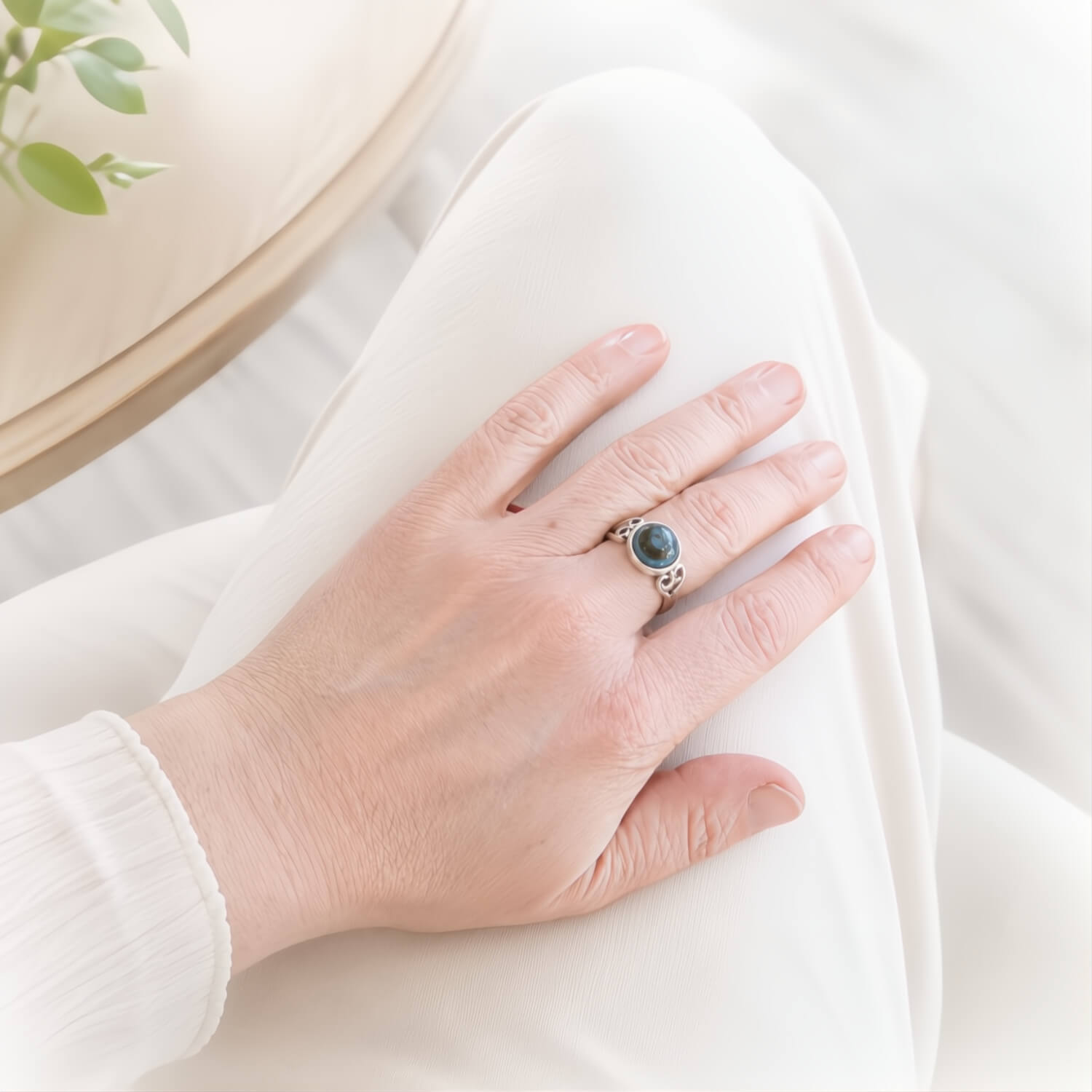 A close-up of a person's hand resting on white fabric, wearing a silver ring with a round blue-green stone.