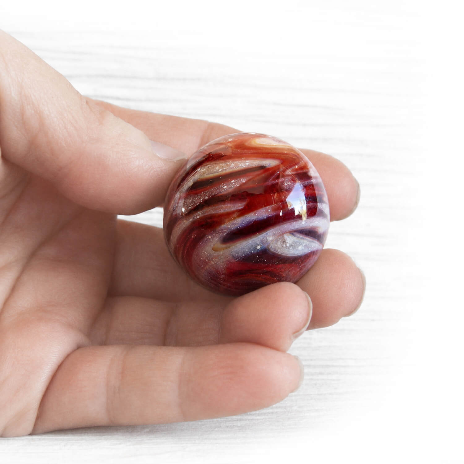 Hand holding a red memorial marble hand crafted from red hand blown glass infused with cremation ashes