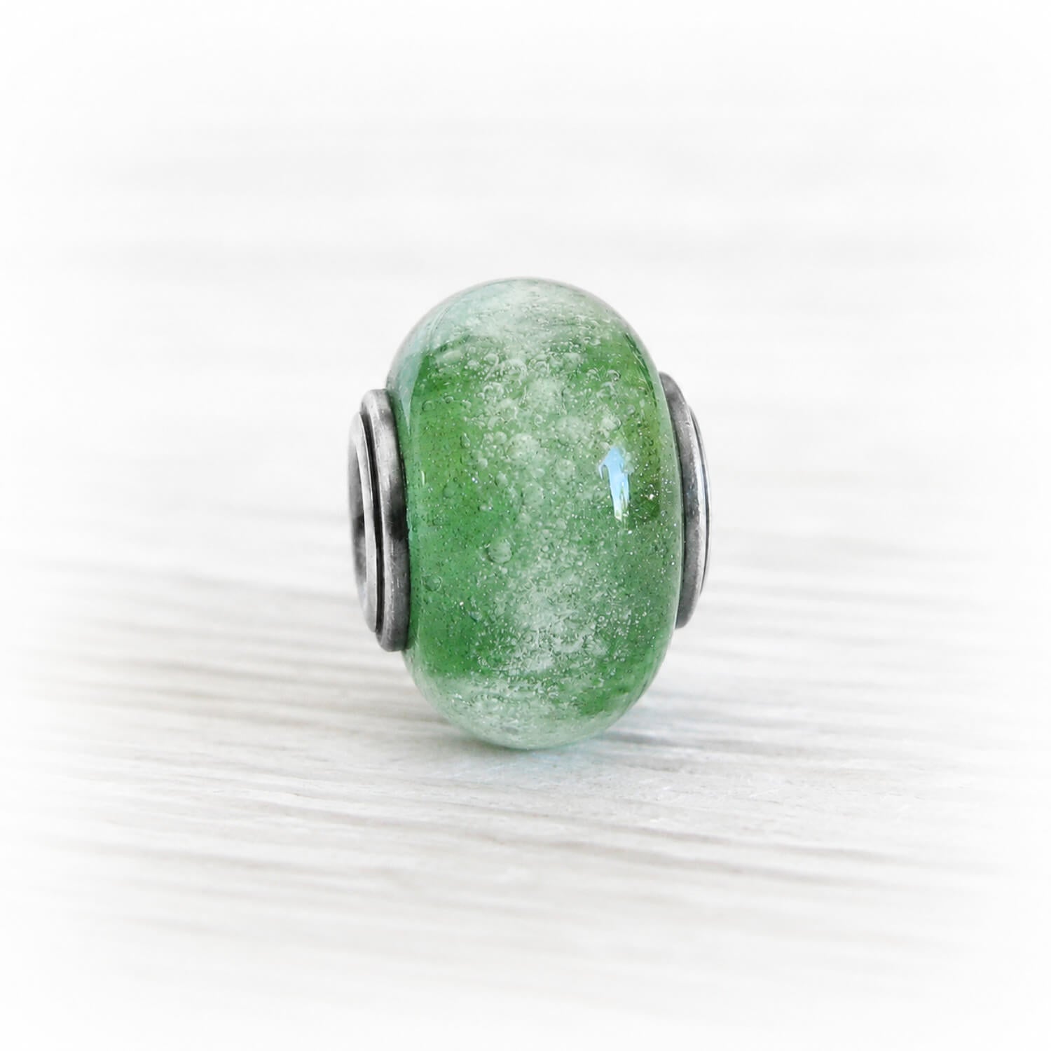 Cremation ashes encased in a hand blown green glass memorial charm bead set on a sterling silver tube with silver end caps with an antique finish