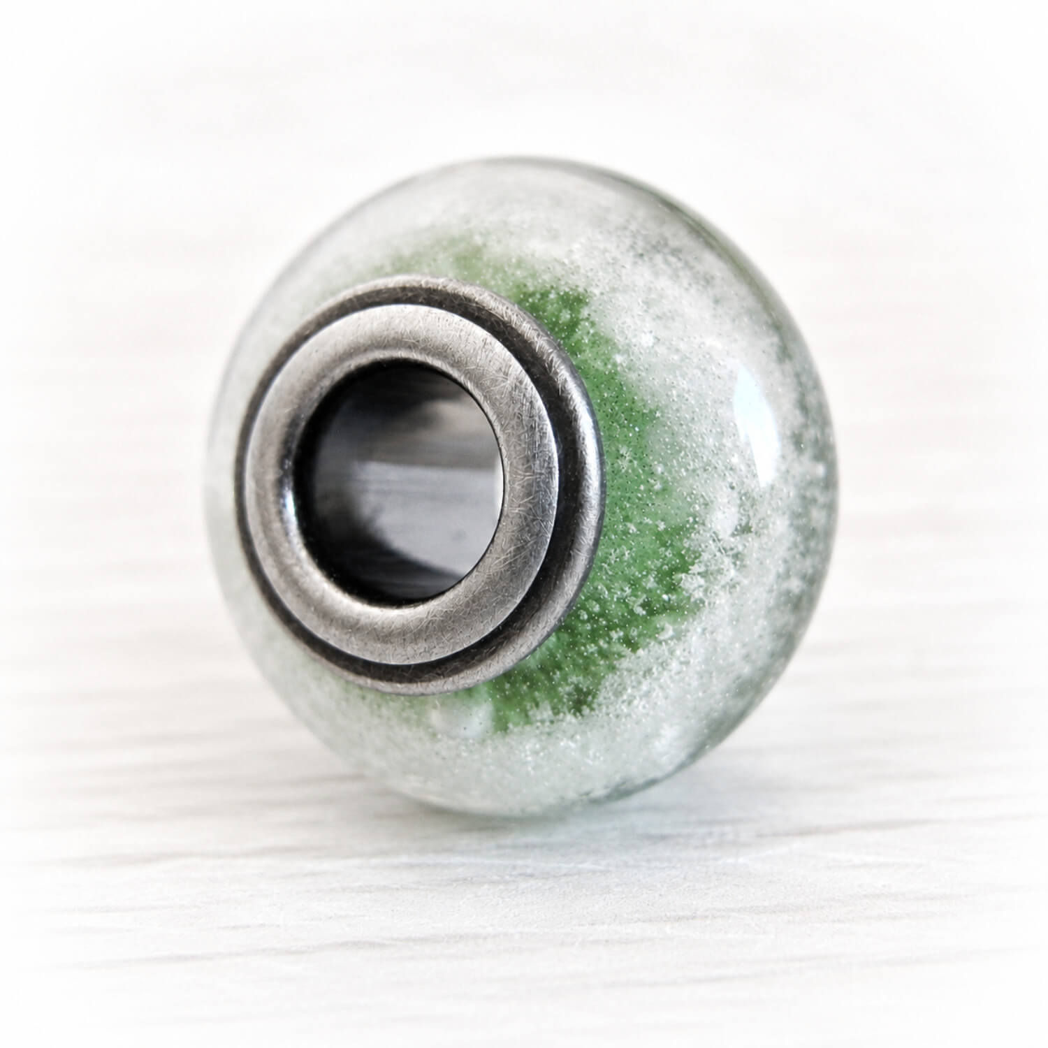 Artisan crafted glass bead with cremation ashes encased and floating over green glass set on dark oxidized sterling silver center