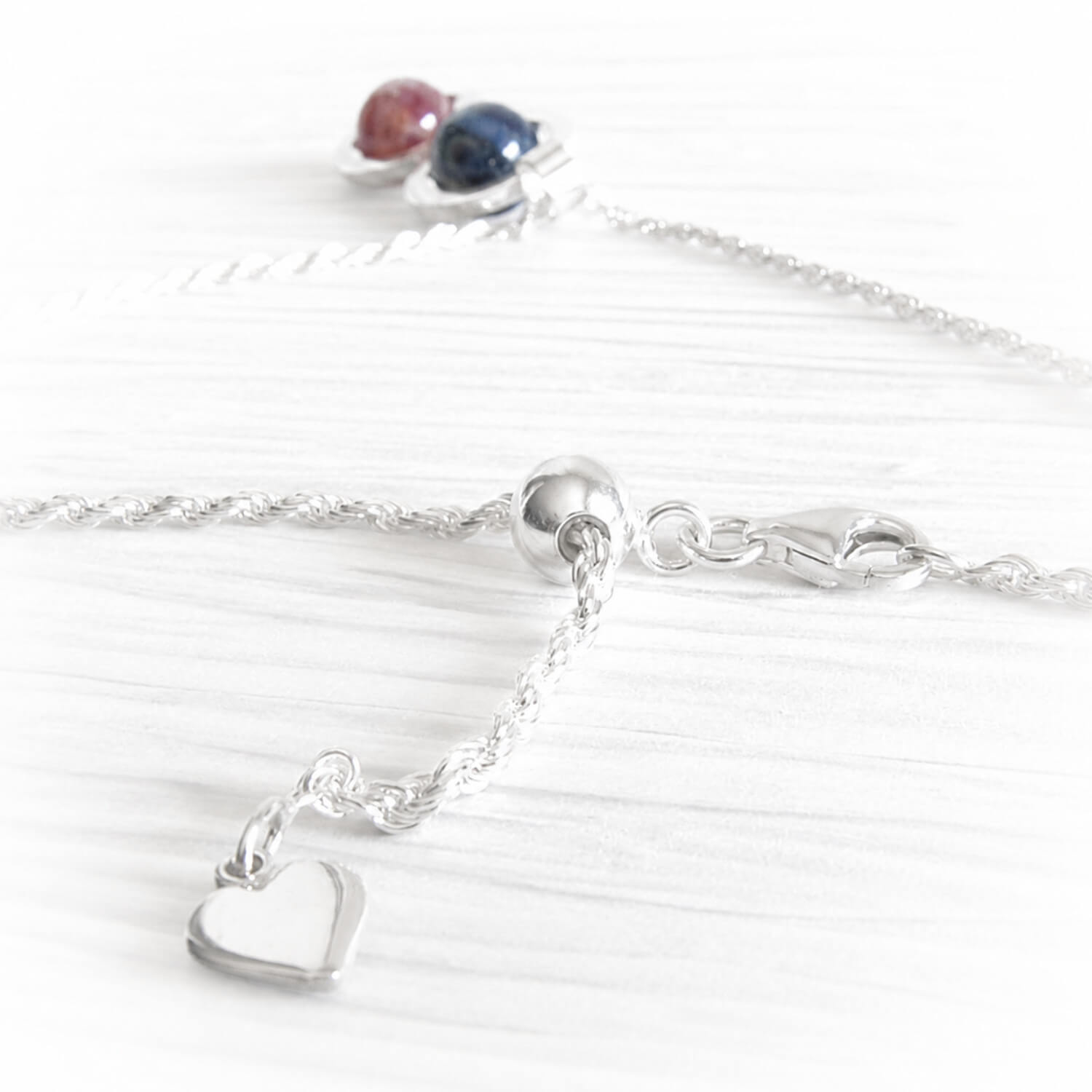 Sterling silver heart charm on a silver adjustable necklace with a memorial pendant in the background