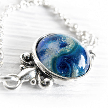 Blue artisan crafted glass swirled with white cremation ashes on a dainty sterling silver memorial necklace