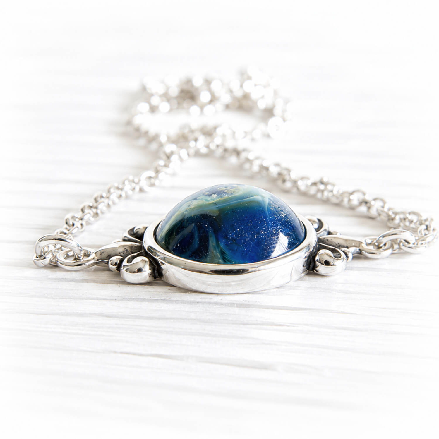 Cremation ashes permanently encased in swirls of blue hand blown glass set in a sterling silver memorial necklace