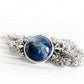 White specks of cremation ashes sealed within blue swirls of hand blown glass in a sterling silver necklace
