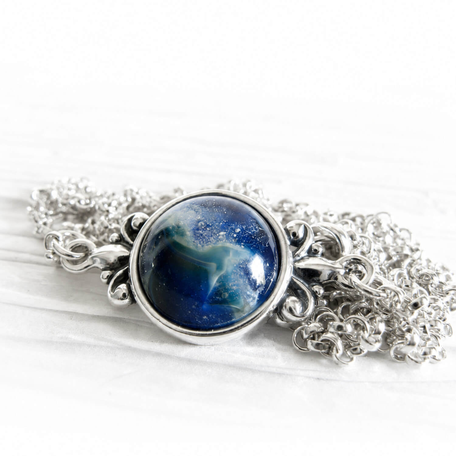 White specks of cremation ashes sealed within blue swirls of hand blown glass in a sterling silver necklace