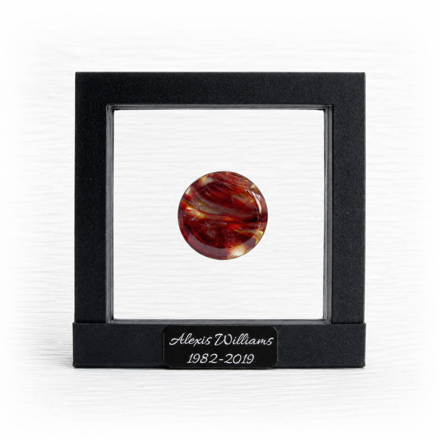 Round red and orange marbled memory stone in a black suspension frame with a personalized engraved nameplate