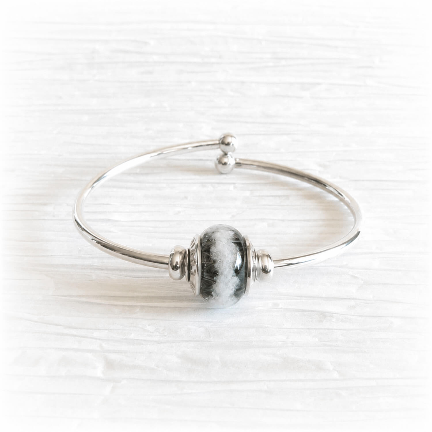 Sterling silver bangle bracelet featuring a artisan crafted glass bead with cremation ashes sealed within the glass
