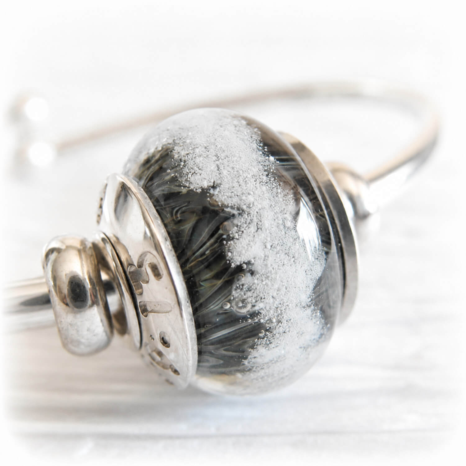 Memorial glass focal bead with swirls of dark grey glass displaying floating ashes visible within the glass