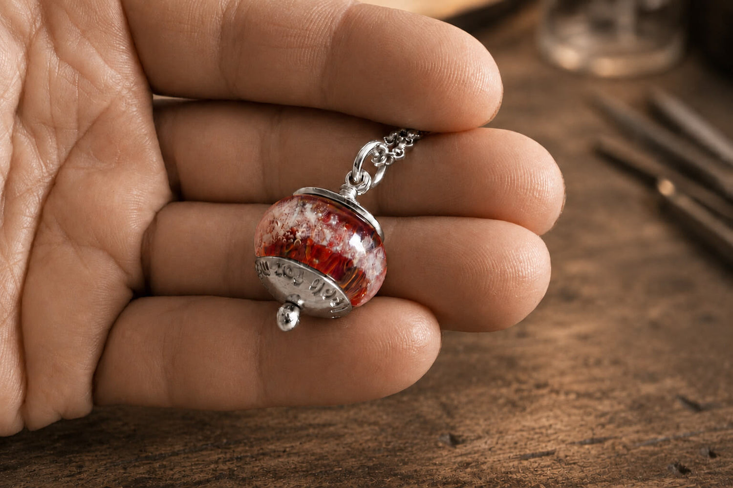 Hand holding a hand blown glass cremation memorial bead on a sterling silver necklace