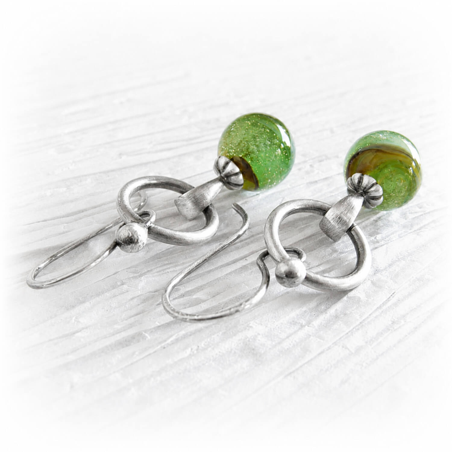 Pair of artisan made earrings featuring glass marbles encasing a loved ones cremation ashes in swirls of green glass
